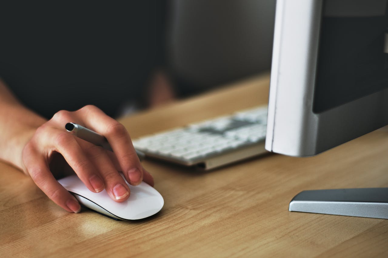 A person using a computer mouse at a wooden desk